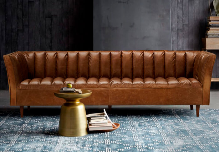 Brown panelled leather couch on grey-blue rug  in living room with dark grey walls